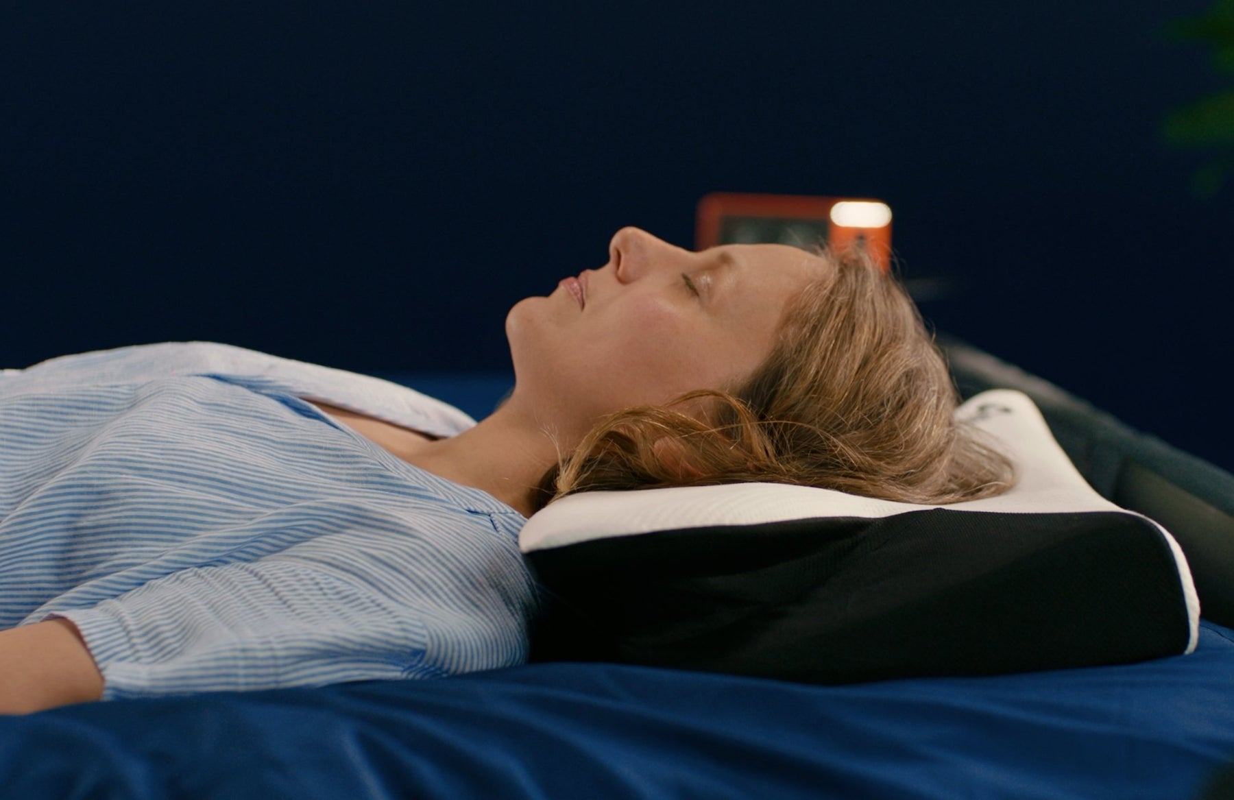 Une femme aux cheveux clairs dort paisiblement sur le dos, la tête reposant sur l'oreiller cervical Cellsius noir et blanc, s Image